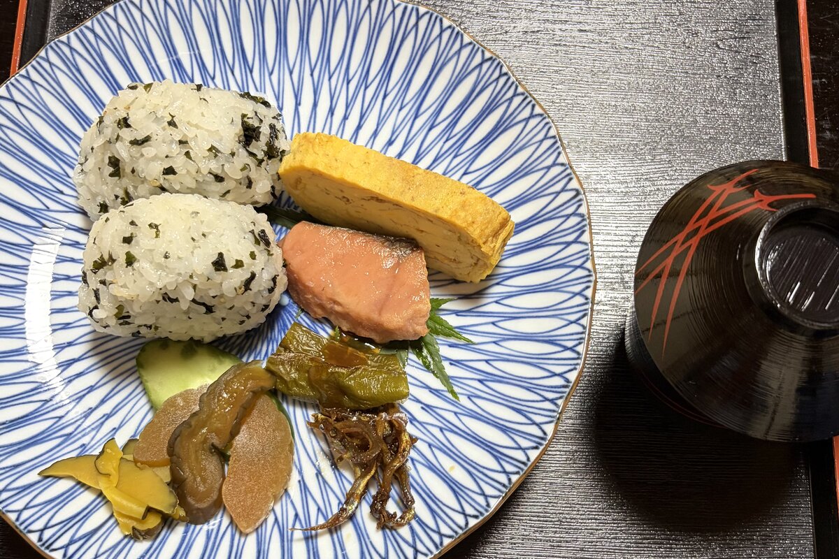 おにぎり、だし巻き卵、鮭、香の物がのった皿と汁椀の朝ごはん
